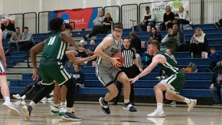 A Penn State Behrend basketball payer dribbles the ball between two defenders.