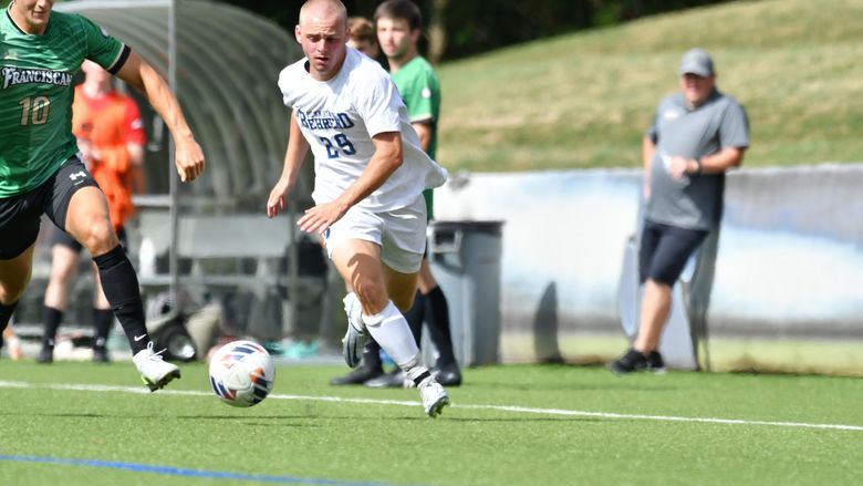 A Penn State Behrend men's soccer player advances the ball up the field.