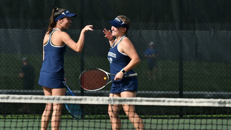 Two Penn State Behrend tennis players congratulate each other after winning a point.