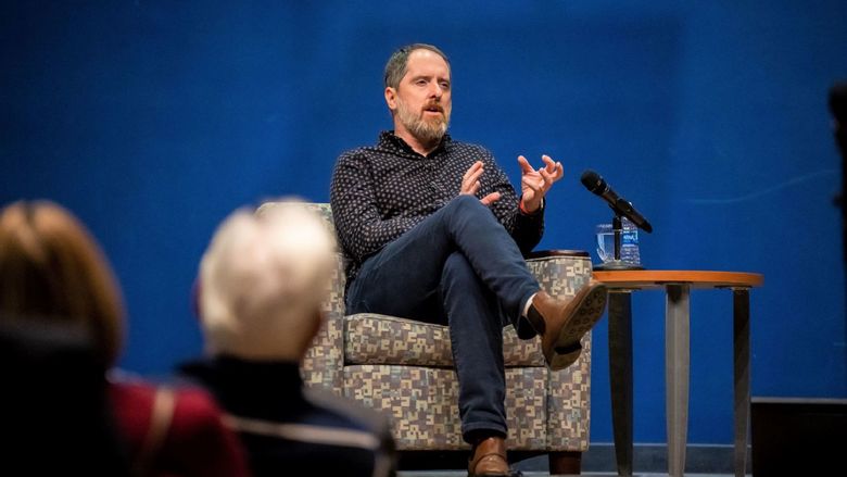 The actor Brendan Hunt gestures with his hands while sitting in a chair on stage at Penn State Behrend.