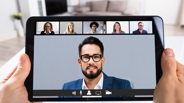 A person holds a tablet computer as it displays faces of Zoom-style meeting participants