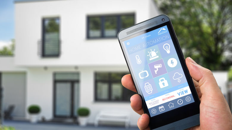 A stock photo of a man holding a smartphone outside a home.