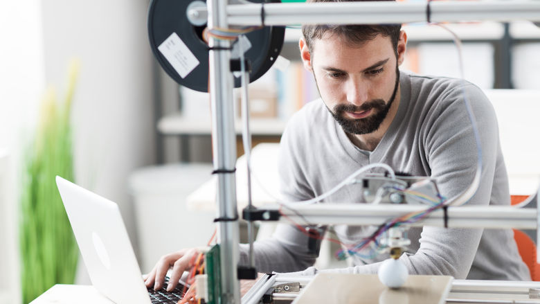 A bearded man works with a 3D printer