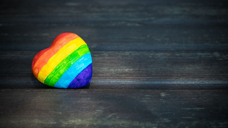 A heart-shaped rock painted with the colors of the rainbow.