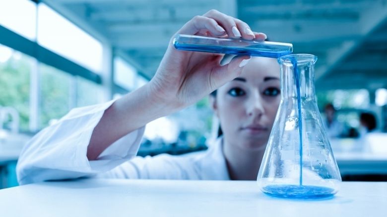 A laboratory researcher pours a blue liquid into a container.