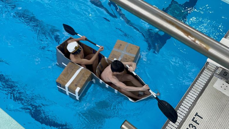 Two people paddle a cardboard boat in Penn State Behrend's pool.