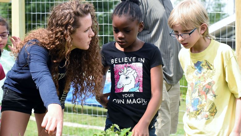 Penn State Behrend student Celeste Makay shows two children vegetables growing in Penn State Behrend's community garden.
