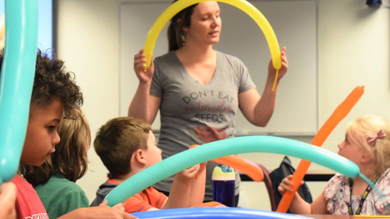 A female instructor bends a long balloon during a youth summer class about the Macy's Thanksgiving Day parade.