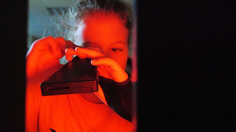 A girl looks through a light spectrum during a science experiment.