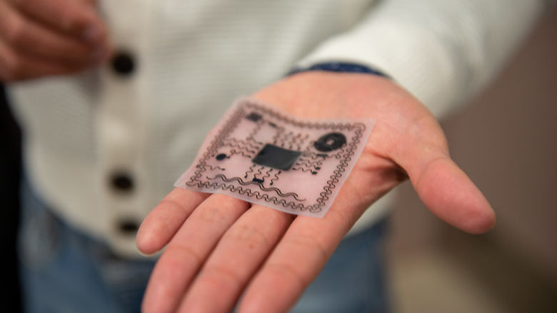 A white membrane with black electronics nestles in the palm of a man’s hand.
