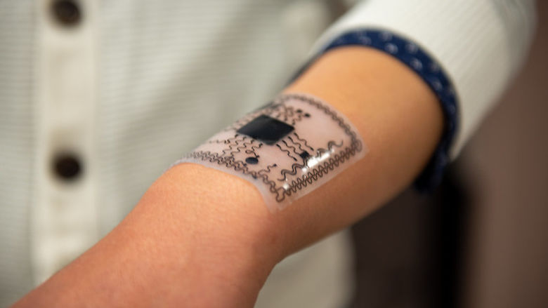 A white membrane with black electronics molds to a man’s forearm. 