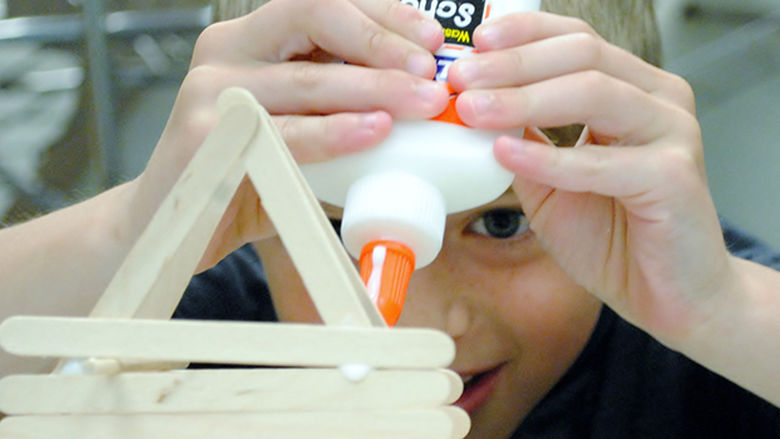 A boy builds an object using popsicle sticks and glue.