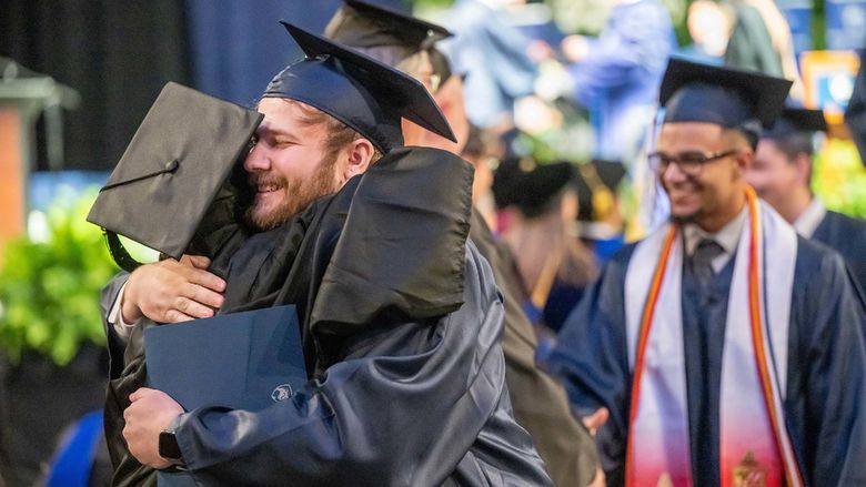 A new graduate hugs a faculty member after leaving the stage at Penn State Behrend's spring 2023 commencement ceremony.