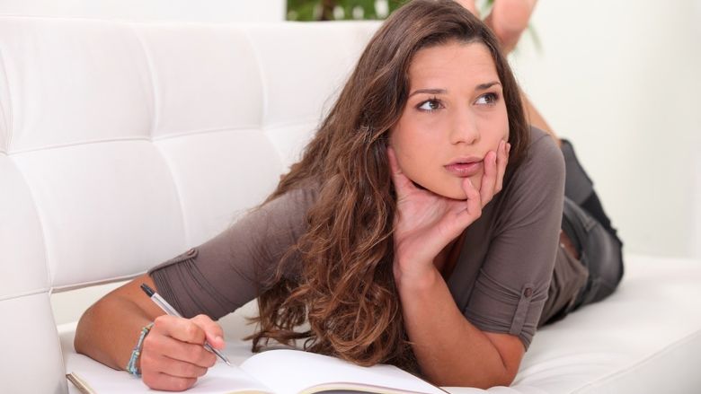 A woman looks to the side while writing in a journal.