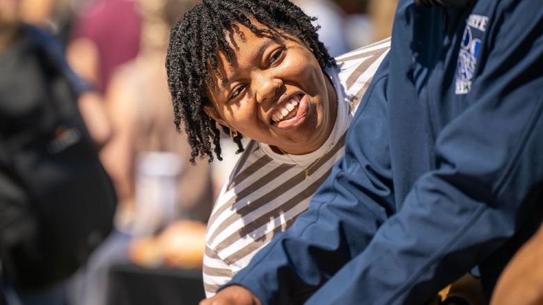 A student leans forward and smiles at another at the Penn State Behrend Discovery Fair, an annual club showcase.