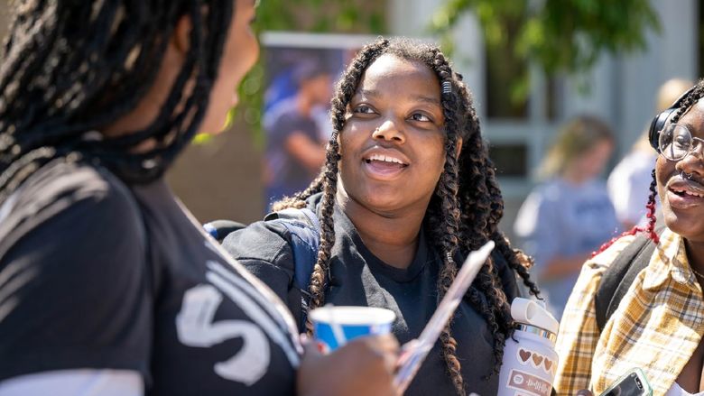 Three female students laugh while talking on the Reed Lawn during Penn State Behrend's Discovery Fair.