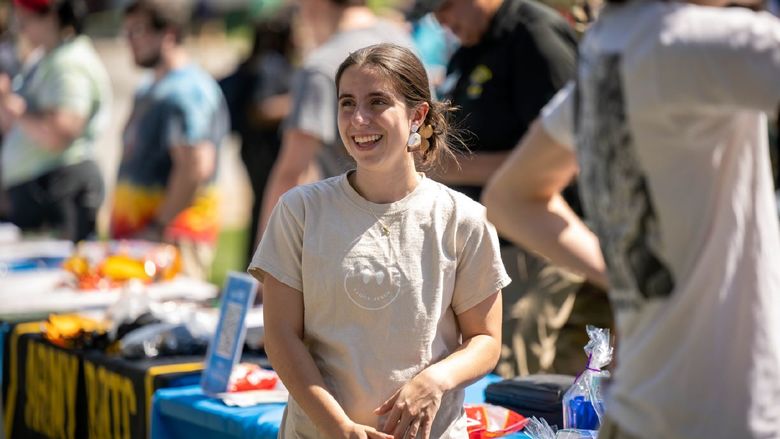 A female student smiles while standing at a table during the Penn State Behrend Discovery Fair.