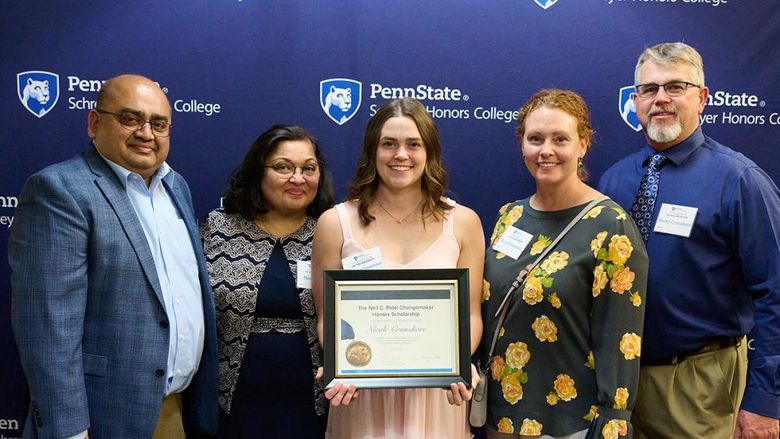 four people in front of a Schreyer banner, person in the center is holding a certificate