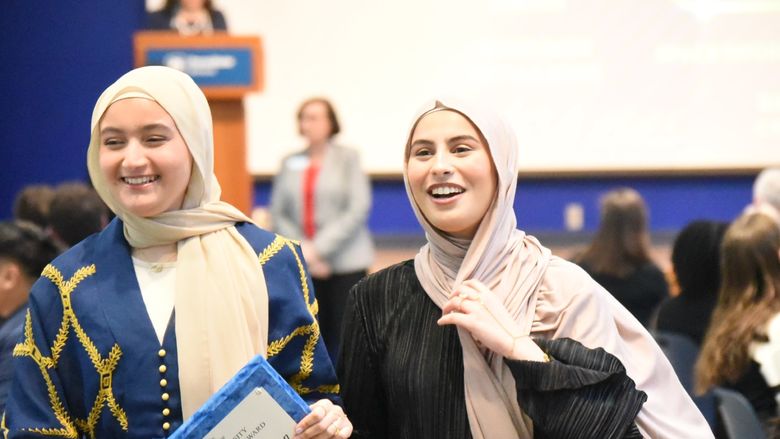 Two women in headscarves carry an award plaque at the Penn State Behrend Excellence in Leadership and Service Awards