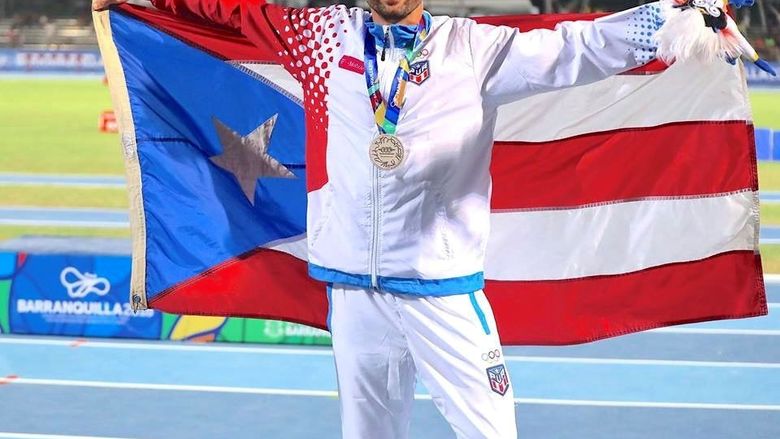 Steeplechase racer Ricardo Estremera poses with the Puerto Rican flag on his shoulders.