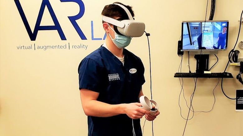 A male student wearing a VR headset experiences a virtual-nursing simulation.