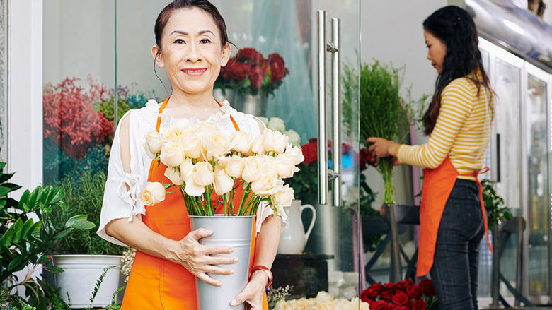 One woman holds white roses, another woman arranges flowers.