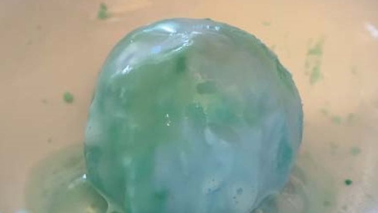 Blue and green ball of baking soda mixture fizzing.