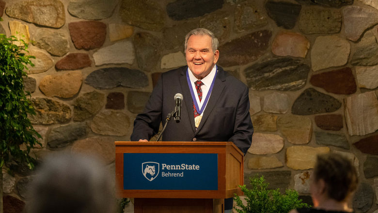 Former Gov. Tom Ridge smiles while standing at a podium at Penn State Behrend.