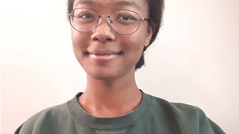 A selfie of Hannah in a green sweatshirt in front of a beige backdrop.