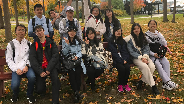 A group of international students outside in fall with trees and leaves that have changed color