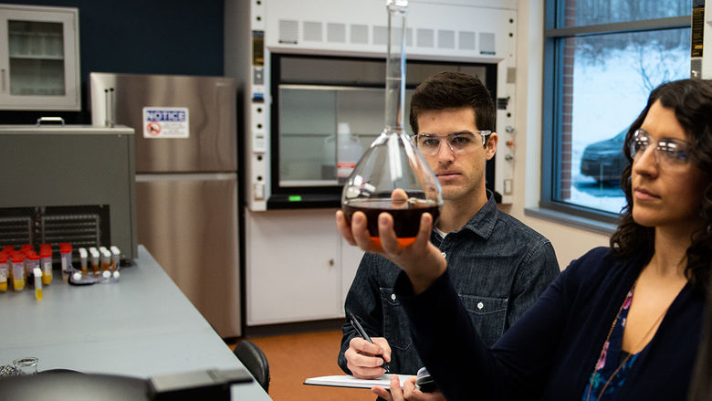 Two researchers examine a liquid in a beaker while working in a chemistry lab at Penn State Behrend.
