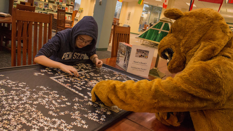 A college student builds a jigsaw puzzle with help from Penn State Behrend's Nittany Lion mascot.