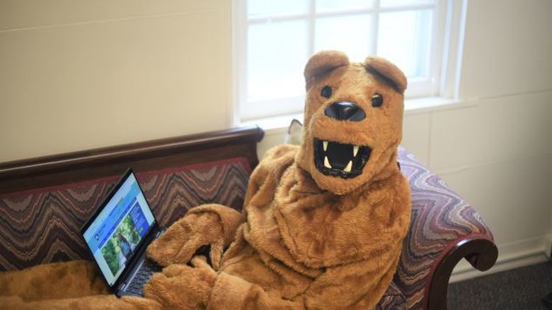The Nittany Lion holds a laptop while reclining on a couch.