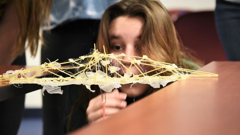 A female student looks closely at a bridge she built with spaghetti noodles.