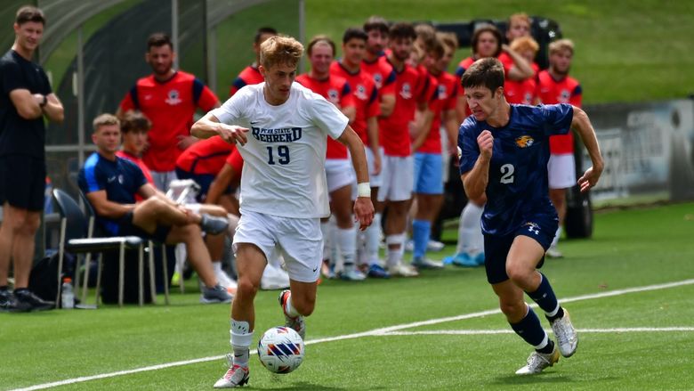 A Penn State Behrend soccer player dribbles the ball past an opponent.