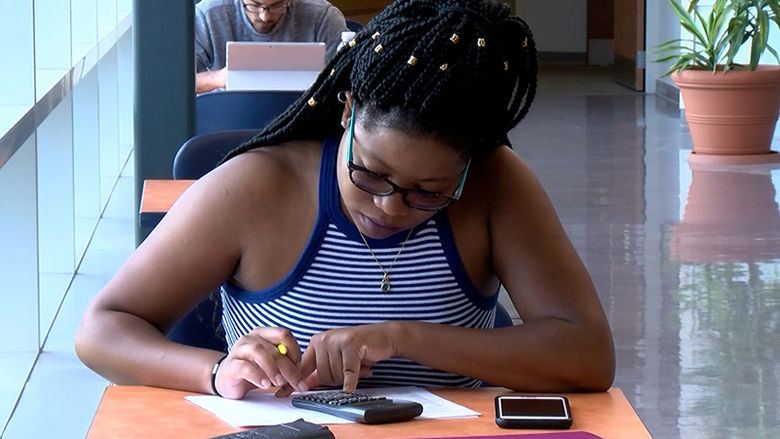 A female student uses a calculator at a study table.