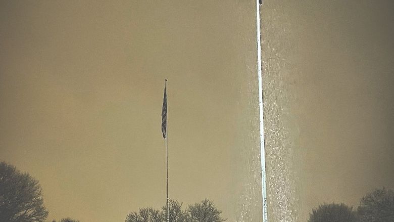 Two tall flag poles with spotlights shining on them, showing the falling snow