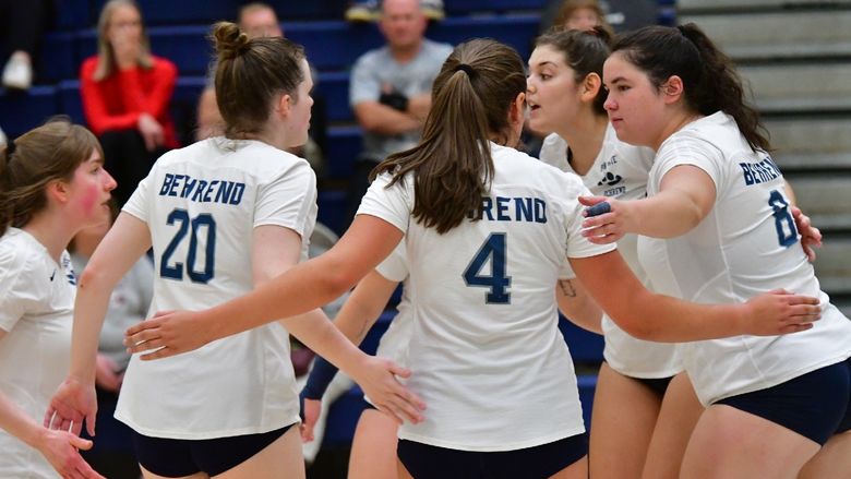 The Penn State Behrend women's volleyball team celebrates in a huddle after winning a point.