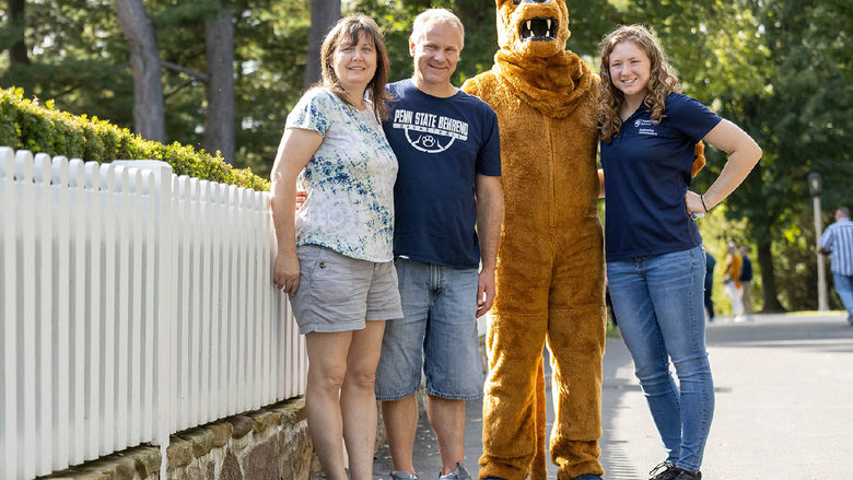 A family poses with the Nittany Lion in front of Penn State Behrend's Glenhill Farmhouse.