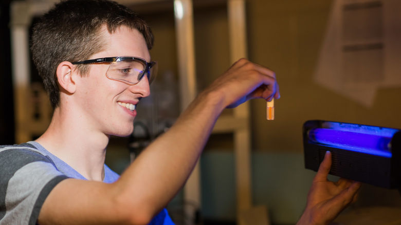 Student holding a glowing orange vial of liquid in front of a blue light.