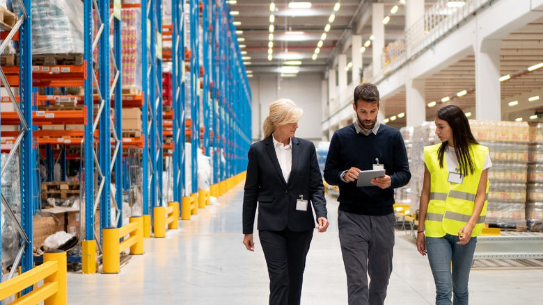 Three people walk in a warehouse.