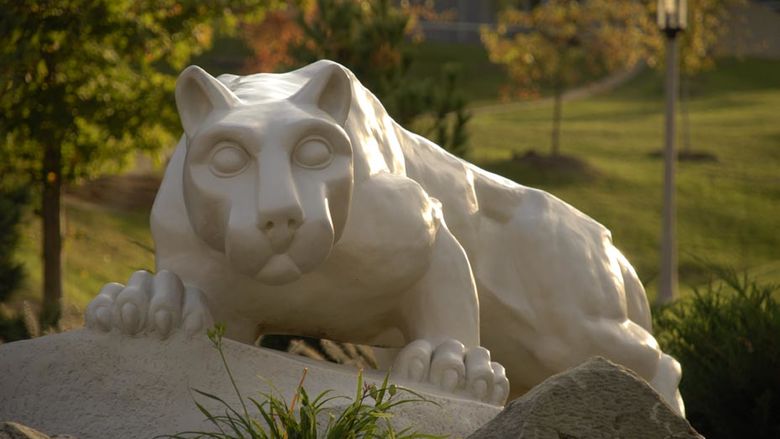 A statue of the Behrend Lion in front of autumn trees
