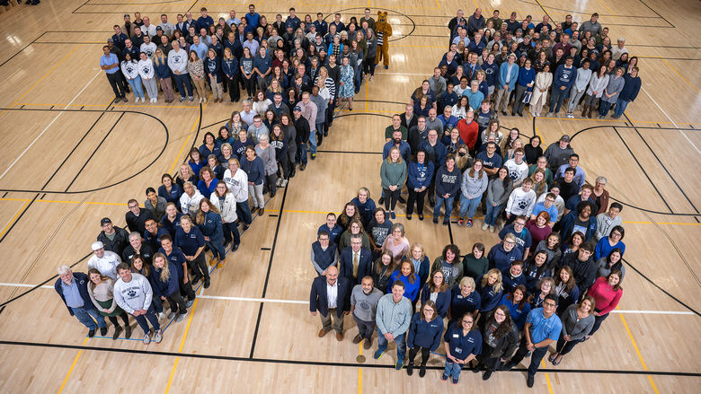 Several hundred people form the number 75 on a gym floor.