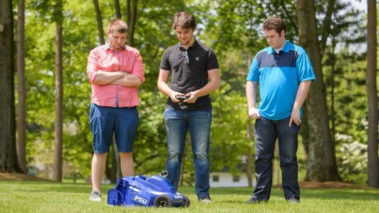 Three Penn State Behrend students operate a remote-control lawn mower.