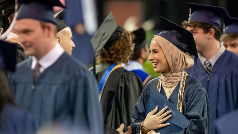 A student in a headscarf holds her diploma at Penn State Behrend's spring commencement program.