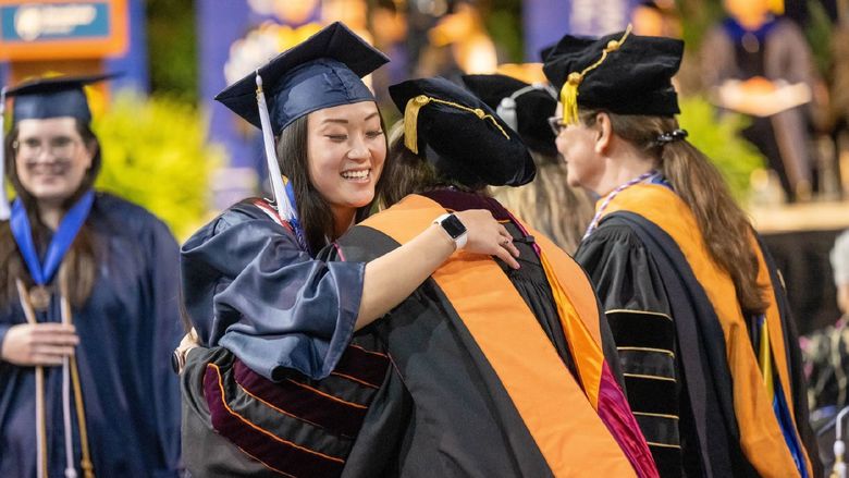 A new Penn State Behrend graduate hugs a faculty member after receiving her diploma.