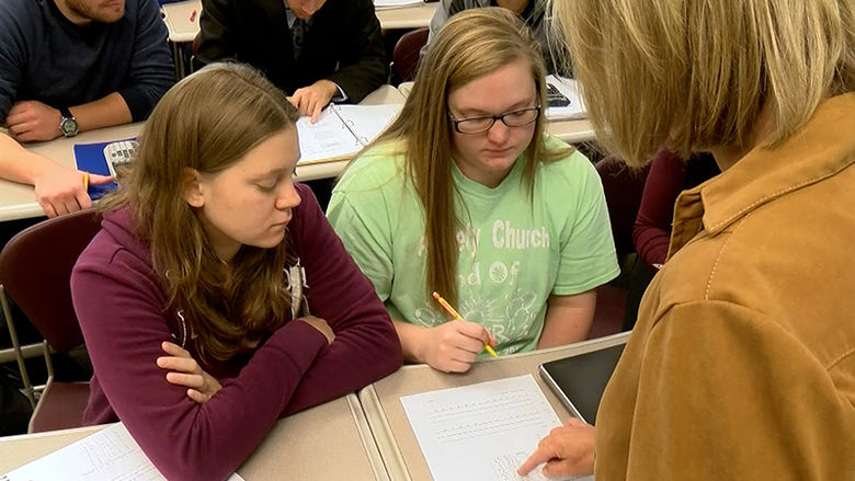 An instructor points out a section of a document to two students in a classroom.