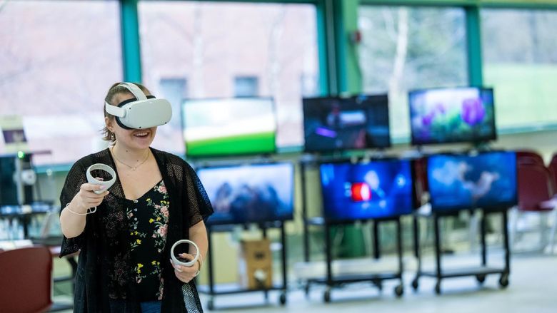 A woman experiments with VR while wearing a headset and holding two controllers.