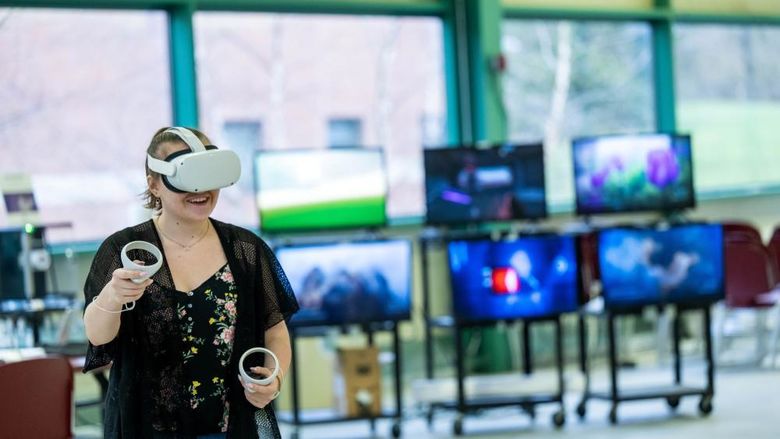 A woman experiments with VR while wearing a headset and holding two controllers.
