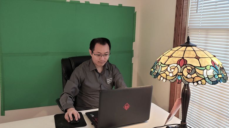 Penn State Behrend professor Richard Zhao works in front of a green screen computer backdrop.